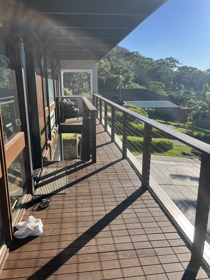 Long balcony deck with a timber-capped wire balustrade in morning sun