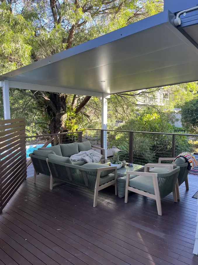 Covered deck under a flat insulated roof, with outdoor lounge furniture, a wire balustrade and a pool below