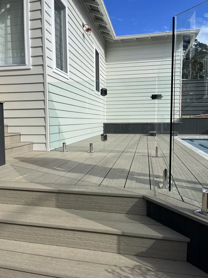 Grey deck boards and steps beside a pool, edged with frameless glass pool fencing