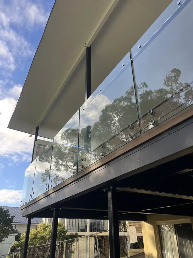 Elevated deck seen from below, with a frameless glass balustrade and a flat roof above