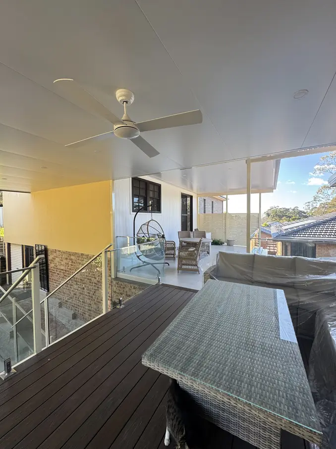 Under a covered patio with a flat insulated roof and ceiling fan, over a deck with glass balustrade